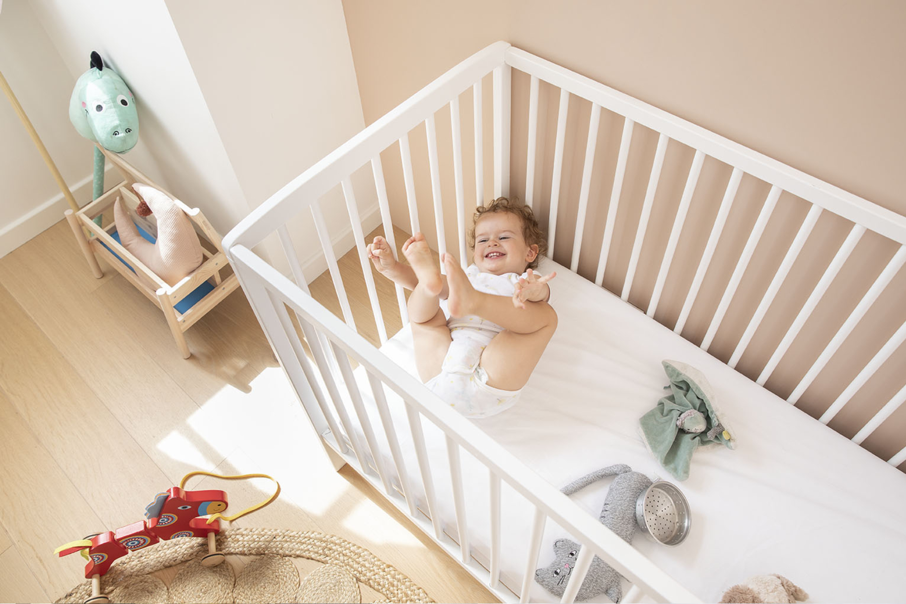Bébé joue les pieds en l'air dans son lit à barreaux sur son matelas Bébé Ilobed.