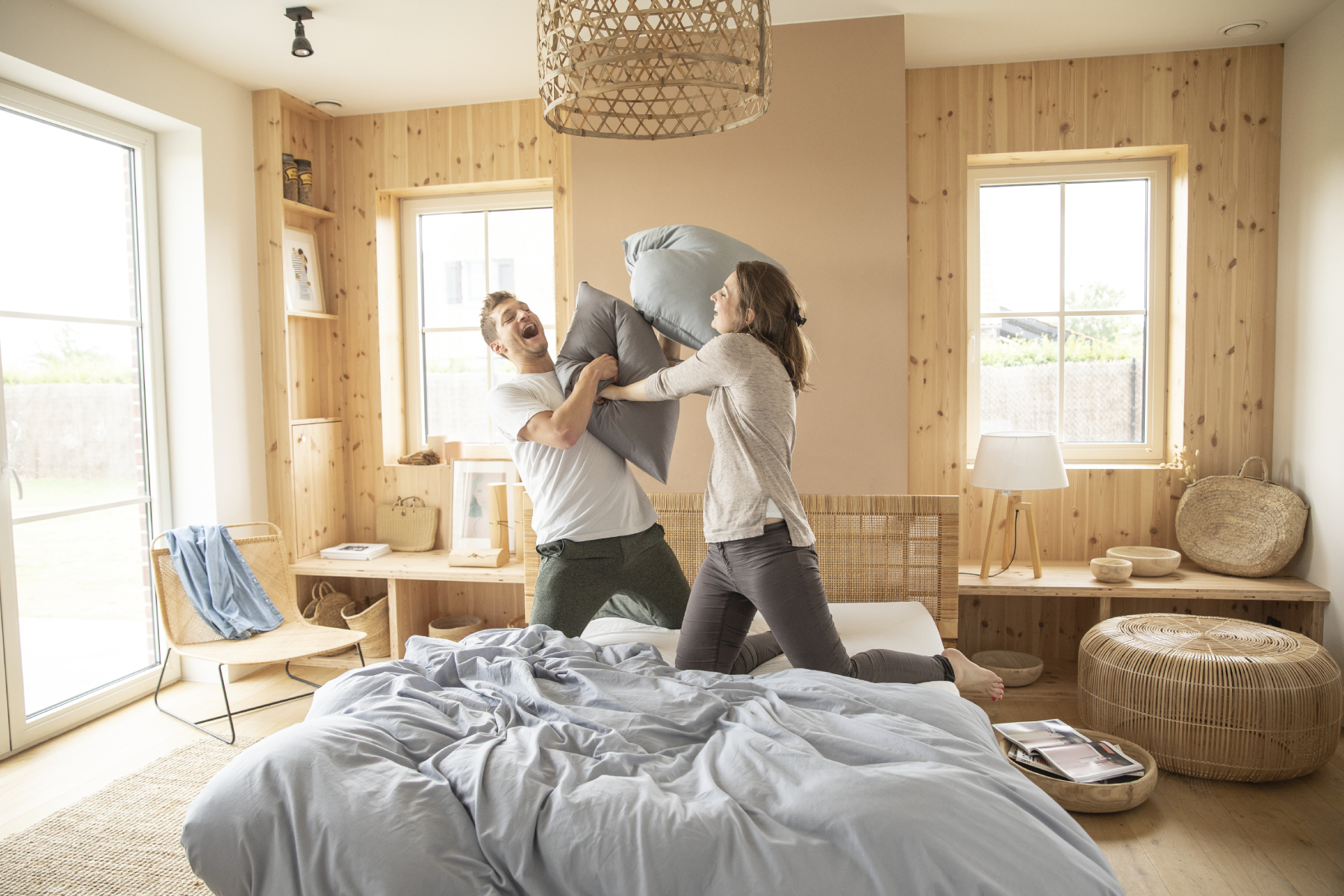 Le matelas Mousse Mémoire et le sommier à lattes Ilobed sont très confortables : un couple fait une bataille d'oreillers dessus dans une chambre cosy.